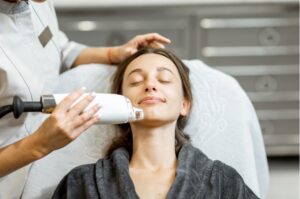 Patient receiving a non-invasive aesthetic treatment on her face, performed by a professional in a spa or clinic setting.