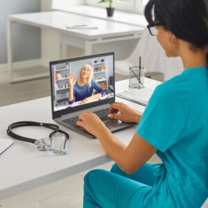 Healthcare professional in blue scrubs conducting a virtual consultation with an elderly woman via laptop, highlighting the use of telemedicine in modern healthcare settings.