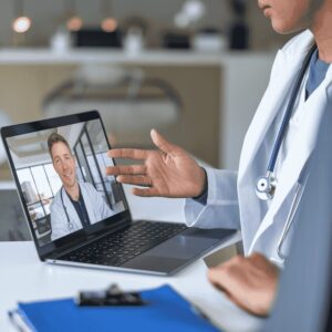 Healthcare provider having a remote video call with a collaborating physician on a laptop, symbolizing remote medical collaboration