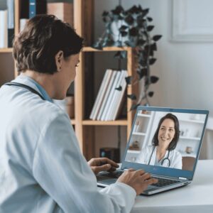 Doctor sitting in front of a laptop, talking to a woman on the screen, illustrating remote physician collaboration with an Advanced Practice Provider.