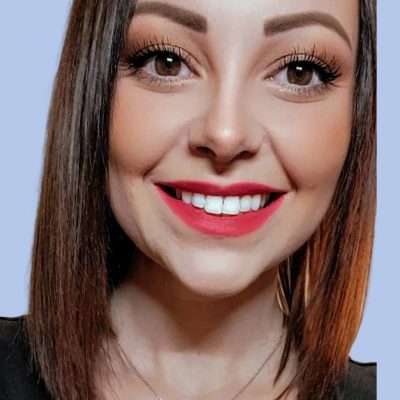 Close-up of a smiling woman with straight brown hair, wearing bright red lipstick, and a necklace, set against a light blue background.